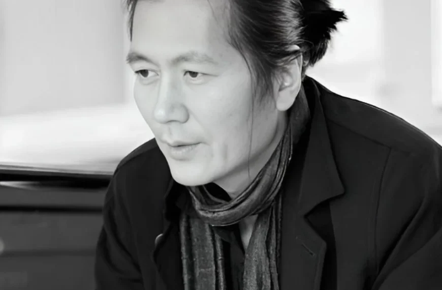 Fotografía de Byung-Chul Han. Muestra a un hombre de mediana edad y rasgos asiáticos, con el pelo negro y liso recogido en una coleta corta baja. Está sentado delante de un piano y mira hacia el suelo lejano a la izquierda de la cámara, con gesto pensativo, como haciendo una pausa mientras habla.