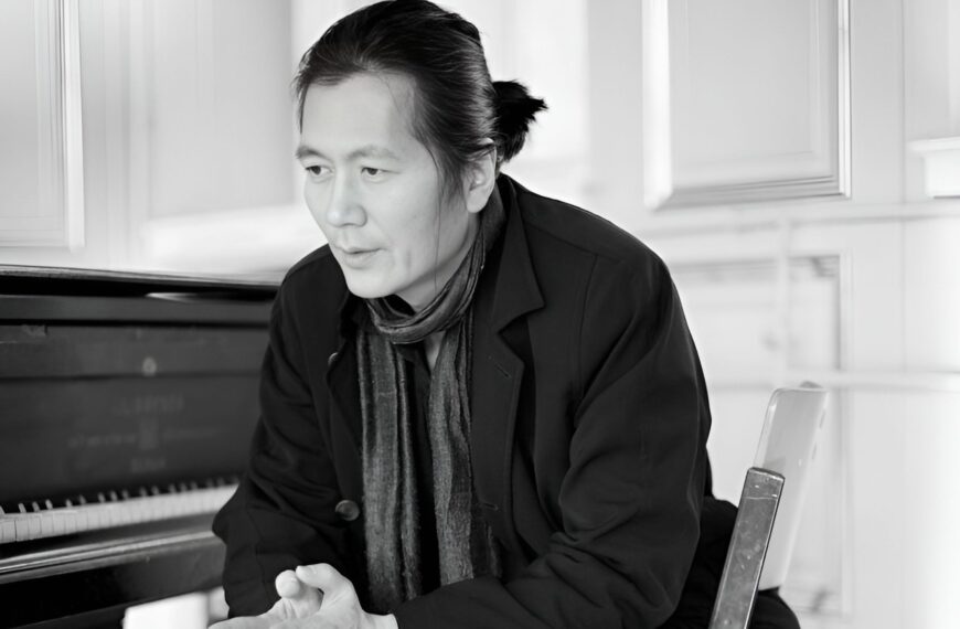 Fotografía de Byung-Chul Han. Muestra a un hombre de rasgos asiáticos, con el pelo negro y liso recogido en una coleta corta baja. Está sentado delante de un piano y mira hacia el suelo lejano a la izquierda de la cámara, con gesto pensativo, como haciendo una pausa mientras habla.