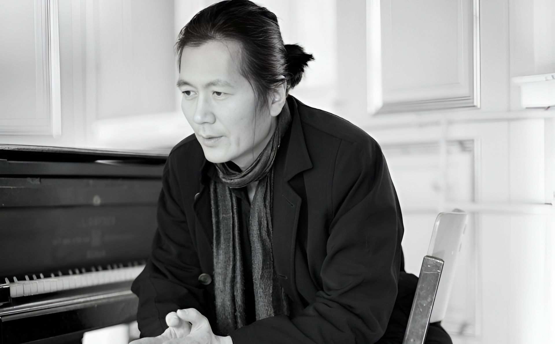 Fotografía de Byung-Chul Han. Muestra a un hombre de rasgos asiáticos, con el pelo negro y liso recogido en una coleta corta baja. Está sentado delante de un piano y mira hacia el suelo lejano a la izquierda de la cámara, con gesto pensativo, como haciendo una pausa mientras habla.