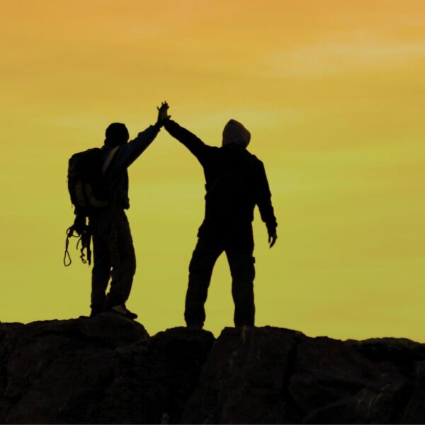 Imagen de la silueta al atardecer de dos amigos en la cima de una montaña felices.
