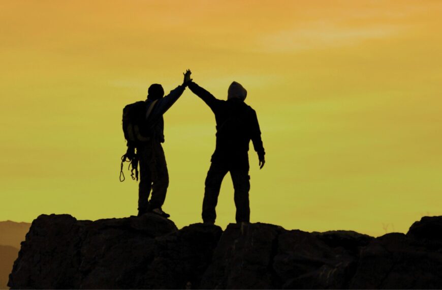 Imagen de la silueta al atardecer de dos amigos en la cima de una montaña felices.
