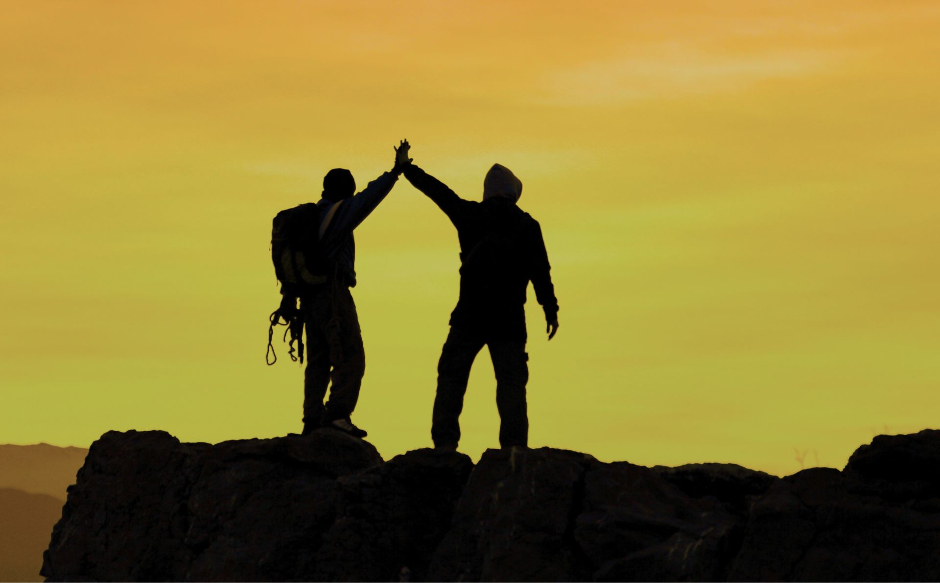 Imagen de la silueta al atardecer de dos amigos en la cima de una montaña felices.